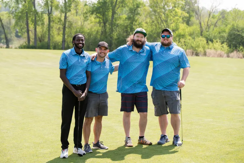 Four Triton team members in branded polos out on a golf course